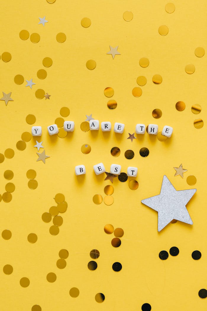 Flat lay of 'You Are The Best' cubes with stars on yellow surface. Motivational decor.
