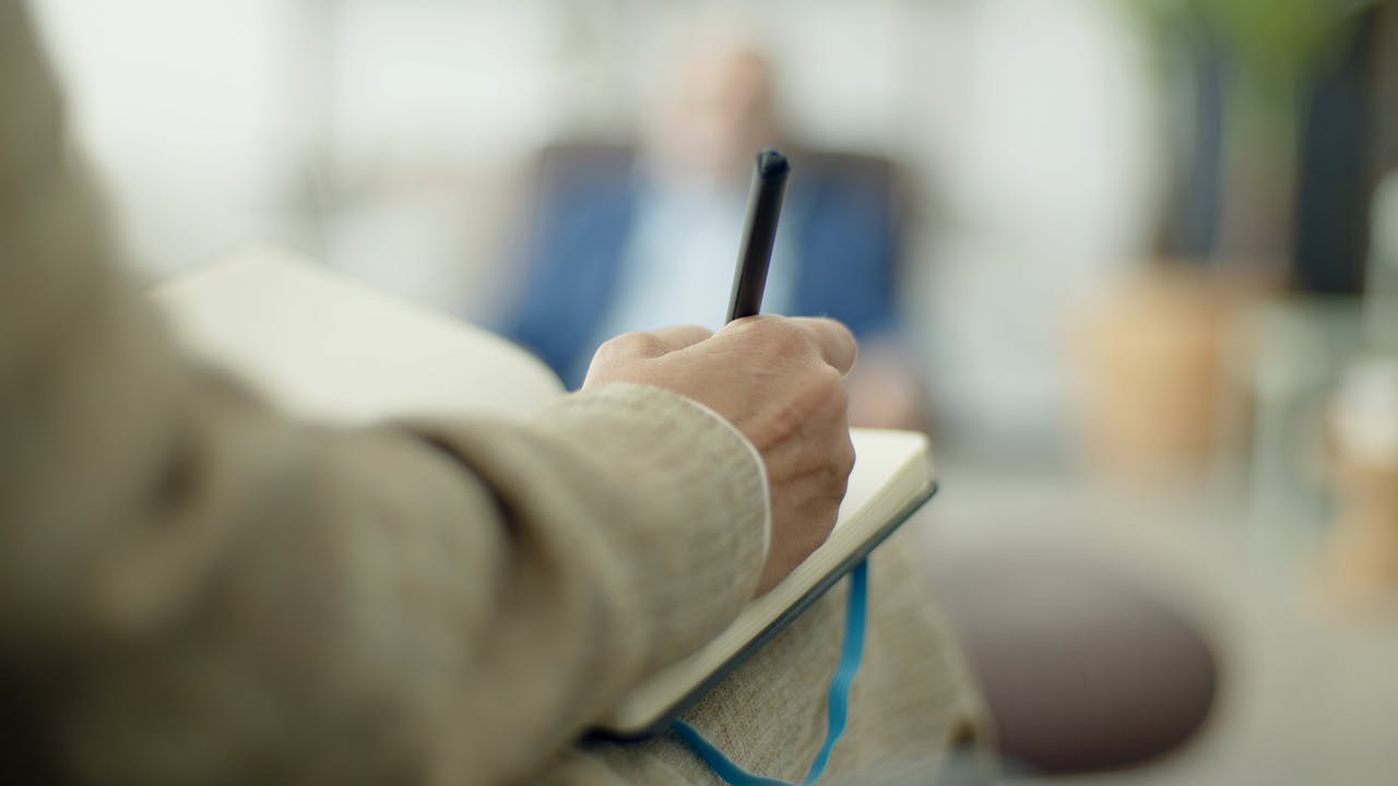 Close-up of an adult writing in a notebook with a pen, depth of field effect.